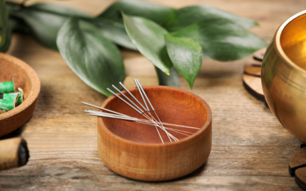 Acupuncture needles in a bowl surrounded by fresh leaves